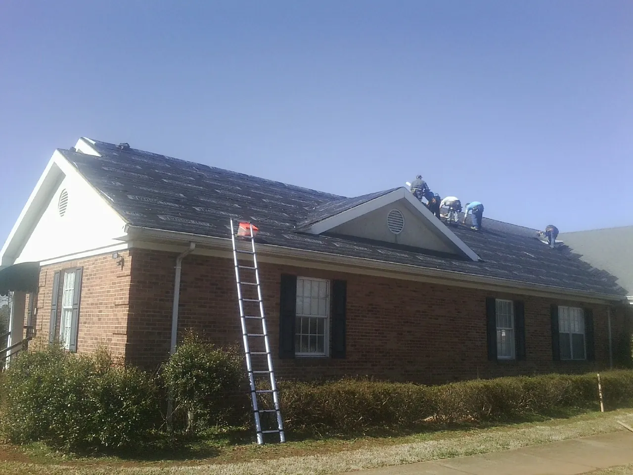 Crew tearing shingles off a brick ranch roof with a ladder set — Metal Roof Repair work by our crew in Lewistown