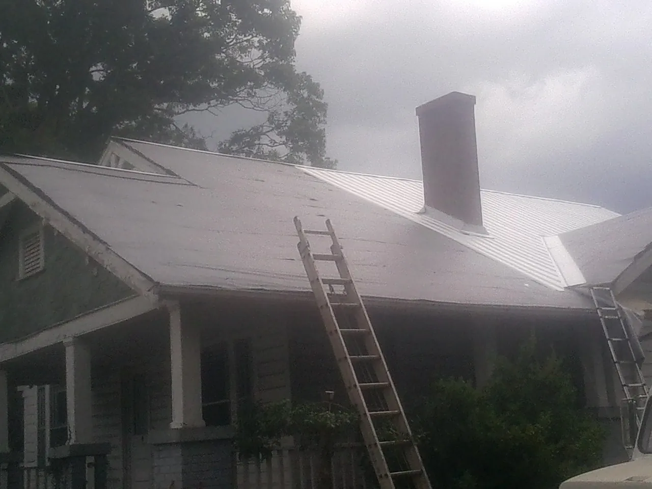 Ladders against a metal roof on an older home with a brick chimney in Lewistown
